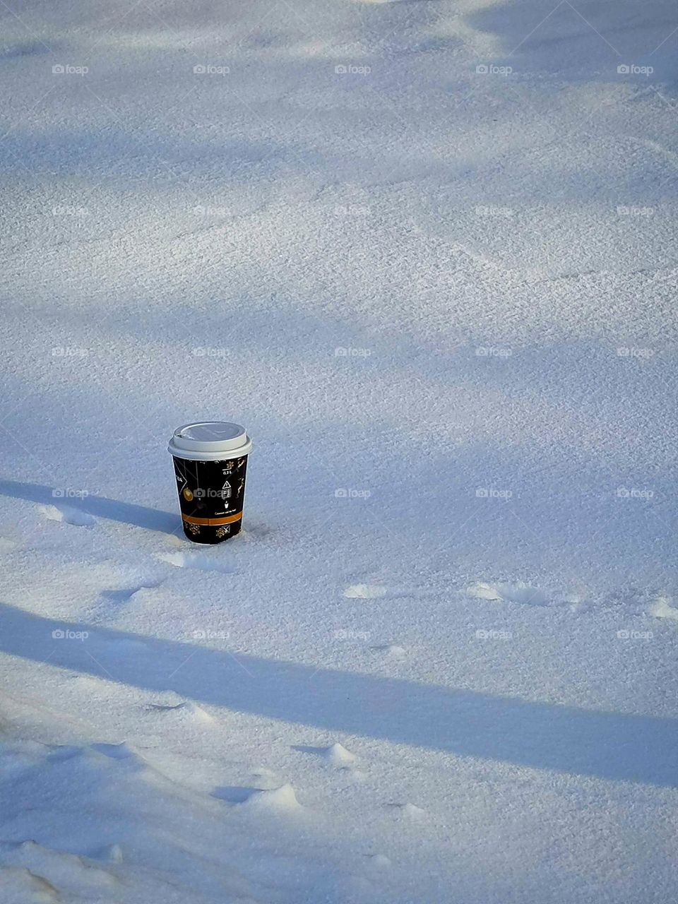 a paper cup with a coffee lid stands in white snow