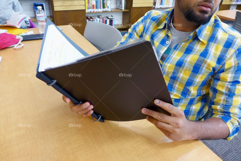 Young adult teenage male student holds notebook while studying in school library 