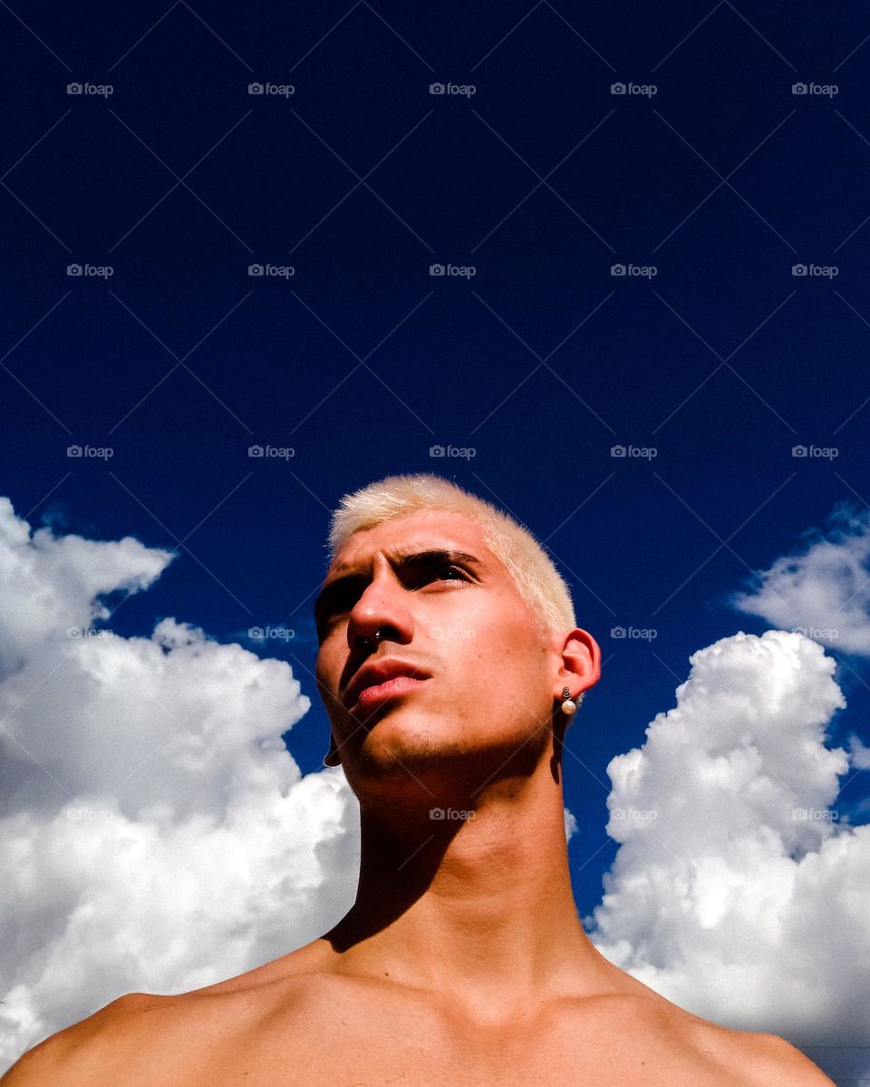Beautiful Selfie Portrait of a blonde man, with an earing, with a gorgeous blue sky and fluffy white clouds on the background