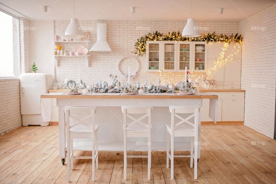 Festive winter cozy kitchen interior with garlands, decorations and gifts.  Christmas dinner at the decorated table.