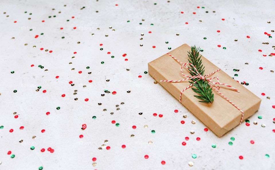 Christmas gift wrapped in brown paper on white background with confetti
