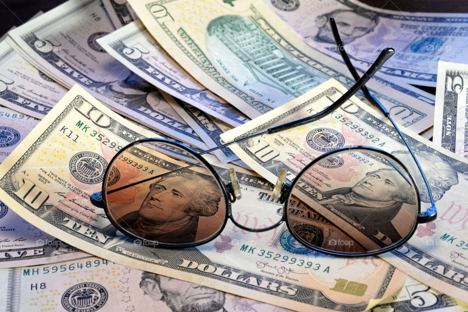 Sunglasses is placed on the banknote of US dollars spread around.