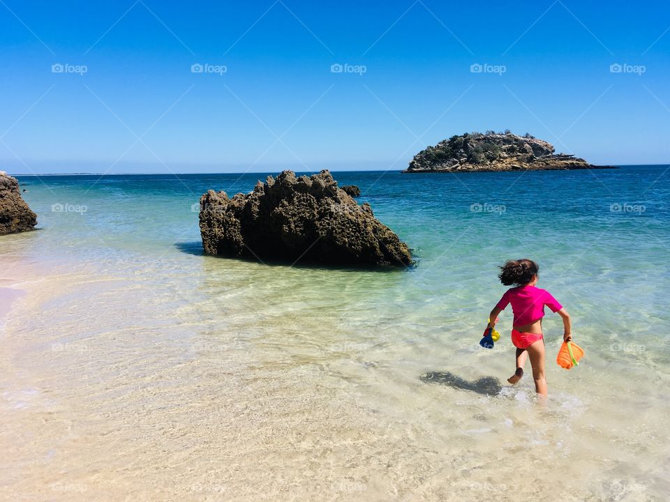 Little girl running and playing in the beach, blue water and sand 