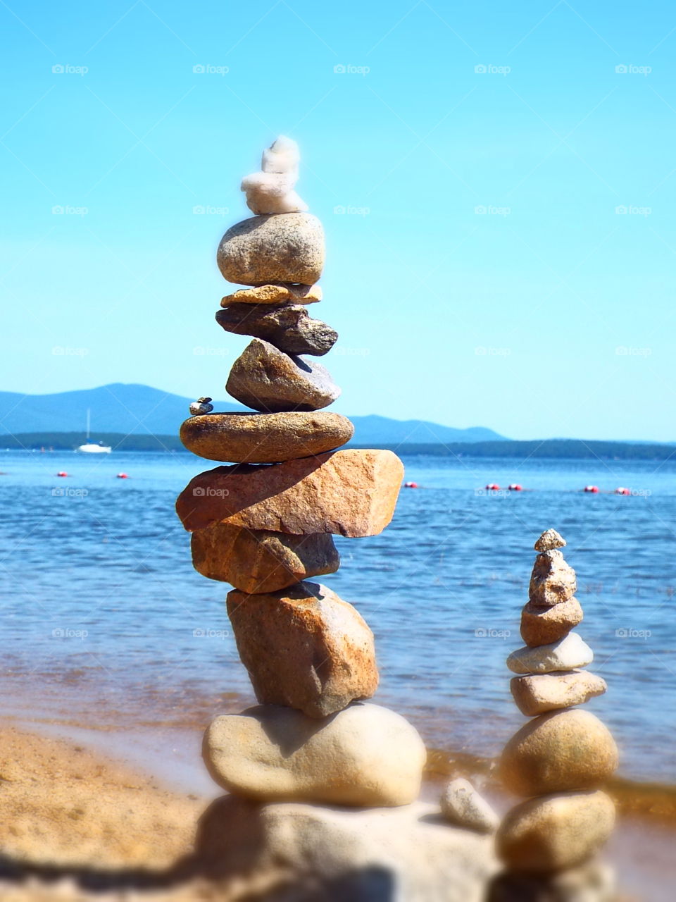 Two rock cairns next to each other on beach with lake in background
