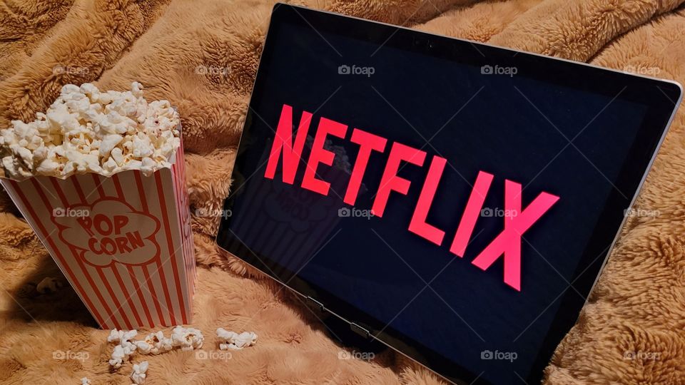 Laptop computer screen ready to watch Netflix for a fun, cozy, and relaxing night with popcorn as a snack, on soft bed blanket in room