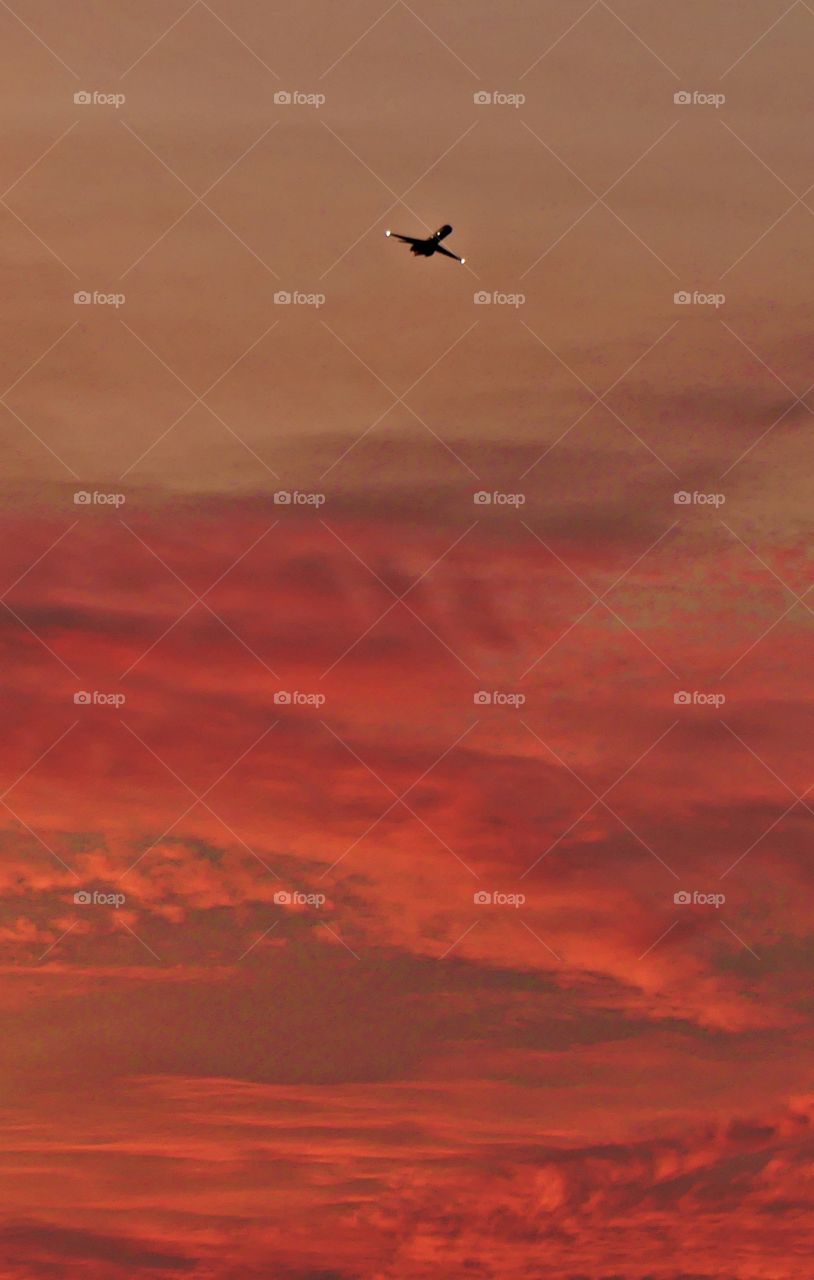 Plane with the lights flying high above the pink, fluffy clouds at sunset 