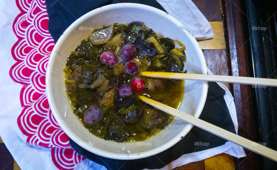 Some oriental style food in a bowl with chopsticks,  topped with red berries