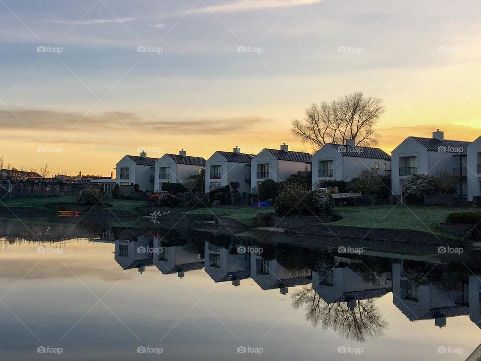 A row of identical luxury houses sit in a line facing the lake and casting a perfect reflection