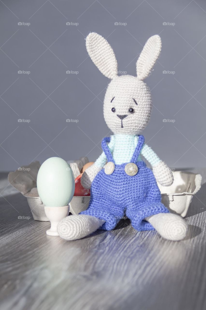 The rabbit of blue color is knitted by own hands at home.  Easter Bunny and chicken egg on coasters.  Craft product.