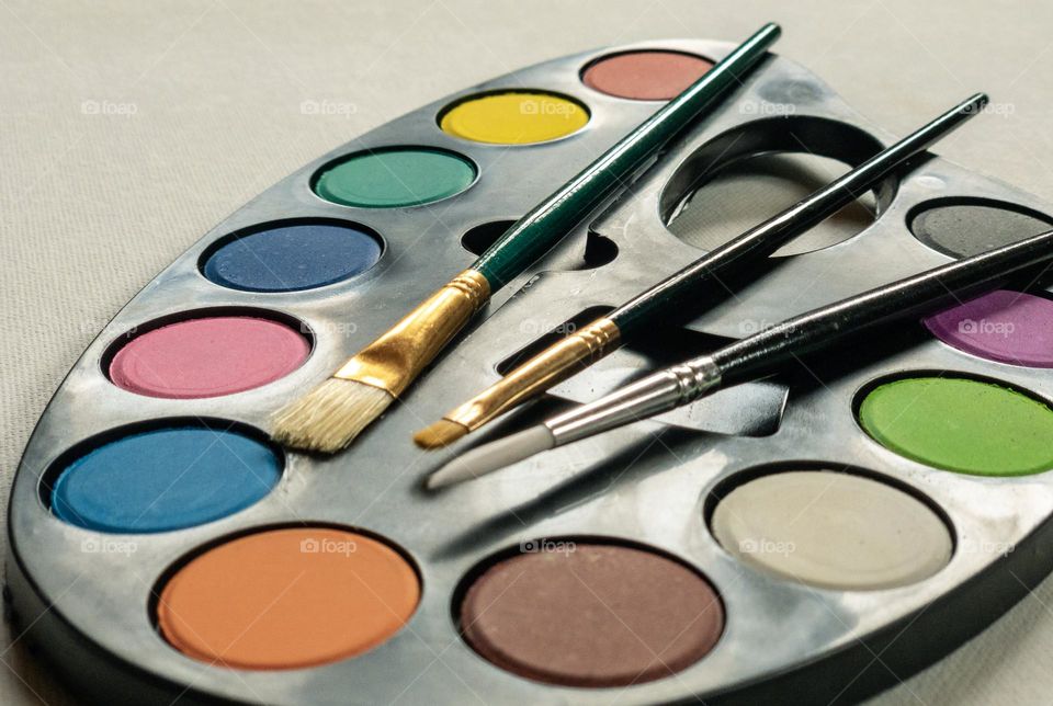 A palette of paints in different colours with assorted paint brushes 