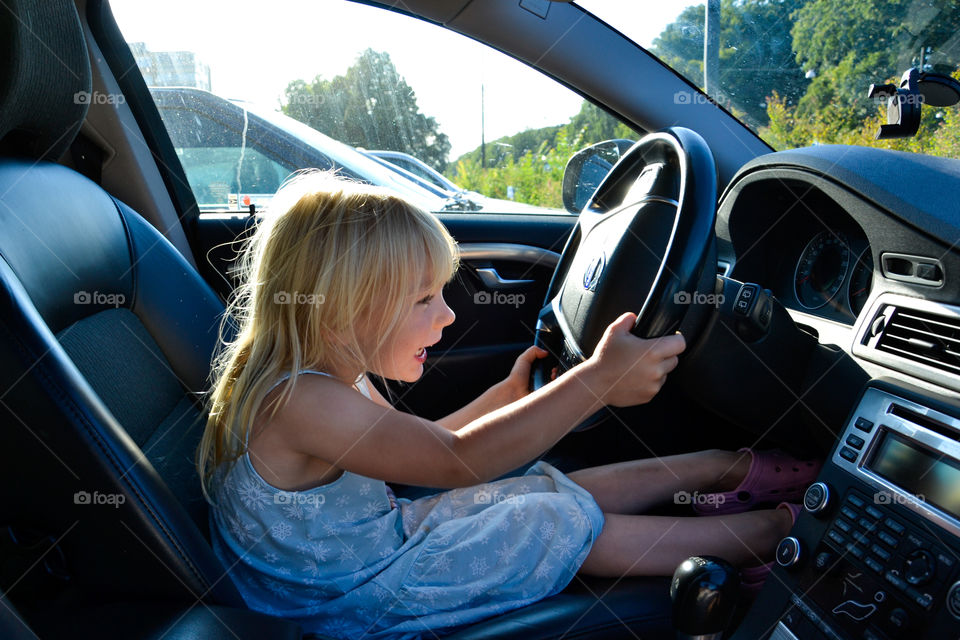 Young girl of five years old trying out driver seat in dads car.