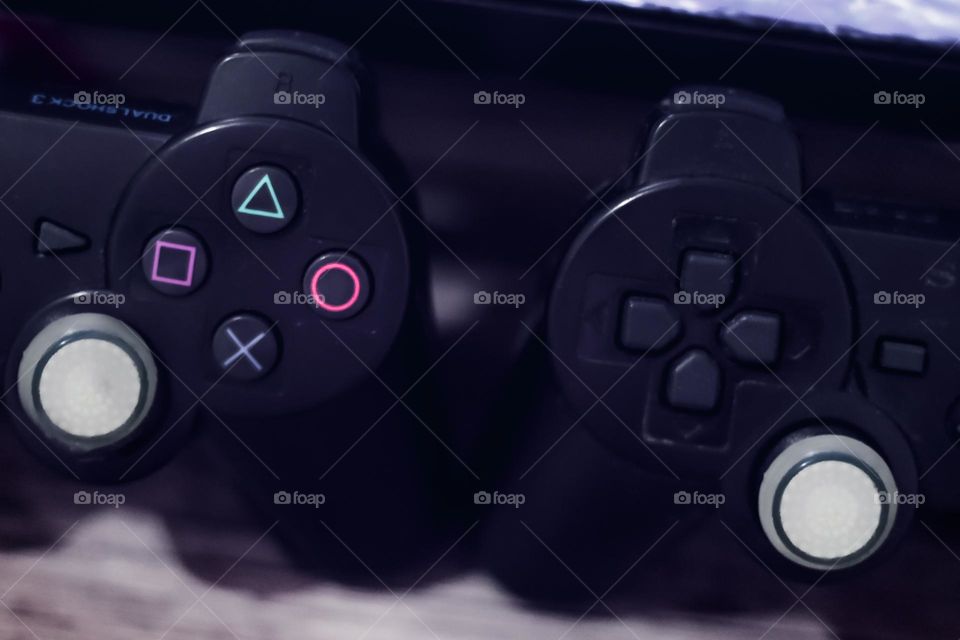 Two playstation gamepad controller on the desk near a TV side by side.