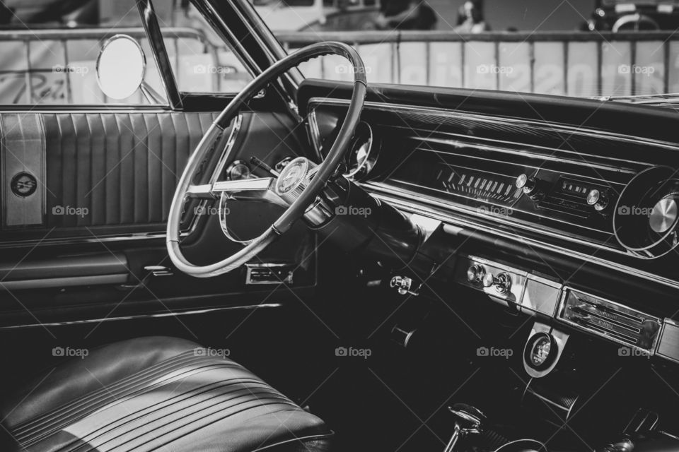 A black and white portrait of the inside of an oldtimer car. the steering wheel and the automatisch gear shifter are visible.