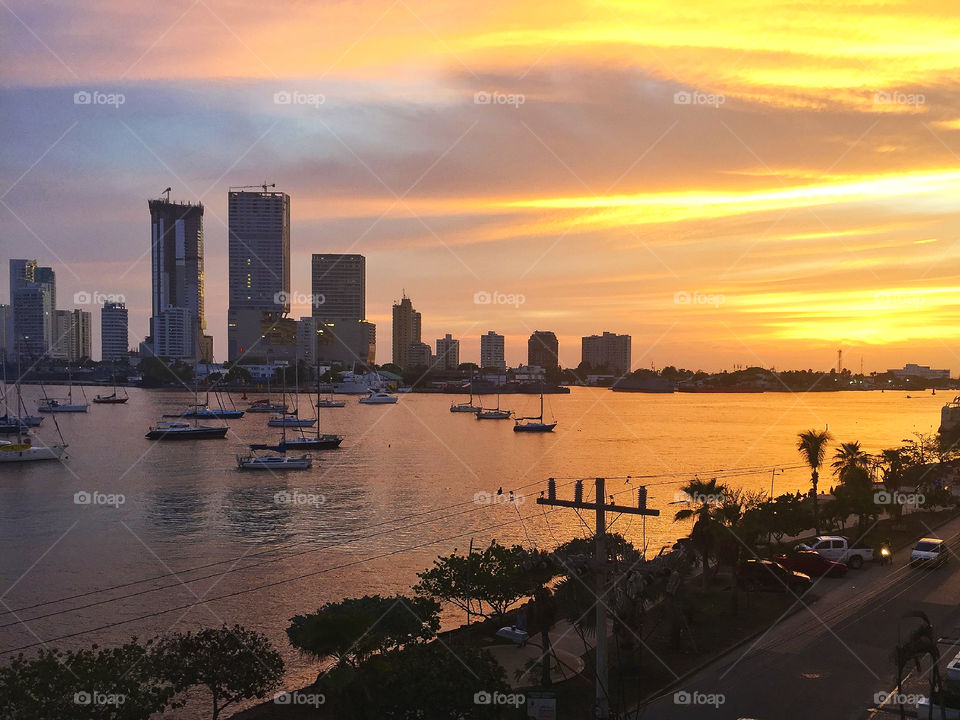 Sailboats in river with urban skyline during sunset