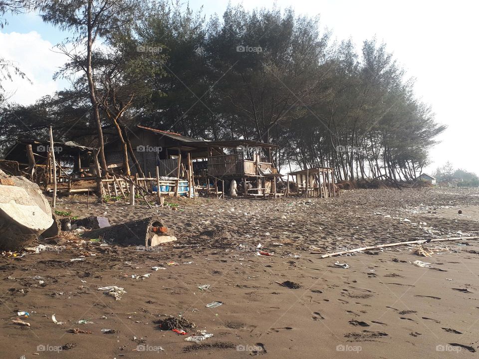 the view on the beach there are wooden houses or kiosks, strewn rubbish and trees lining the coastline in the morning looks very clear
