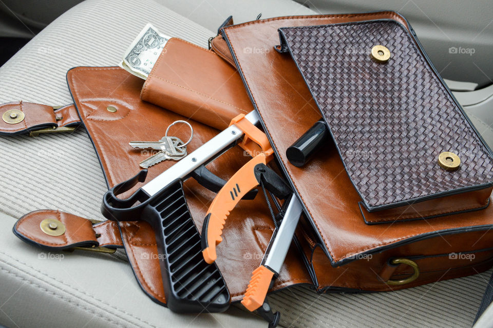 Purse laid out on the seat of a car with a foldable reacher inside