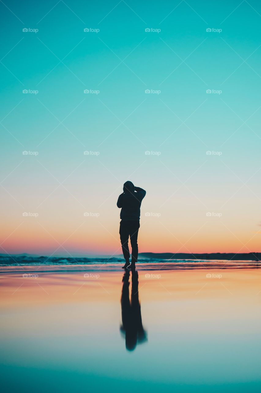 a man standing on the water at Stockton beach with the sunset in the background