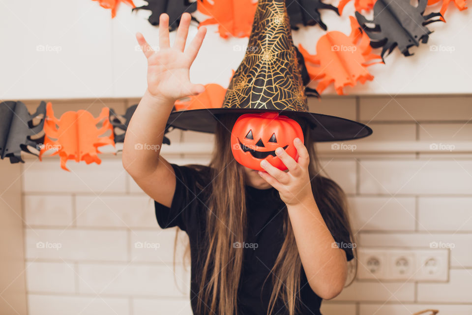 Little girl dressed as a witch for halloween holding a pumpkin with a face on the background decor