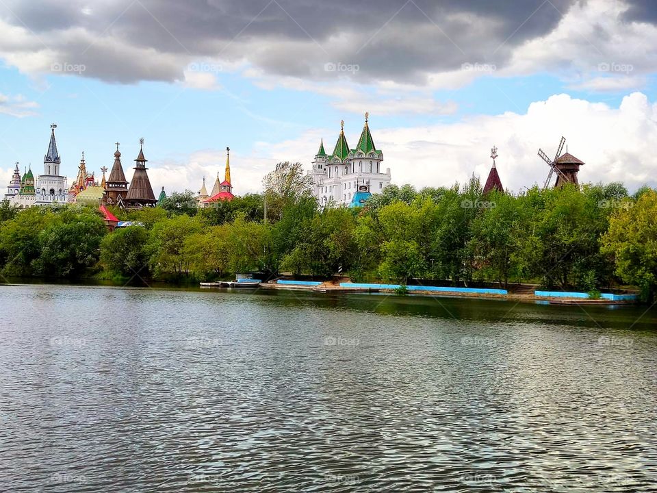 Summer day.  River.  Clouds over the domes and towers that are visible among the green trees