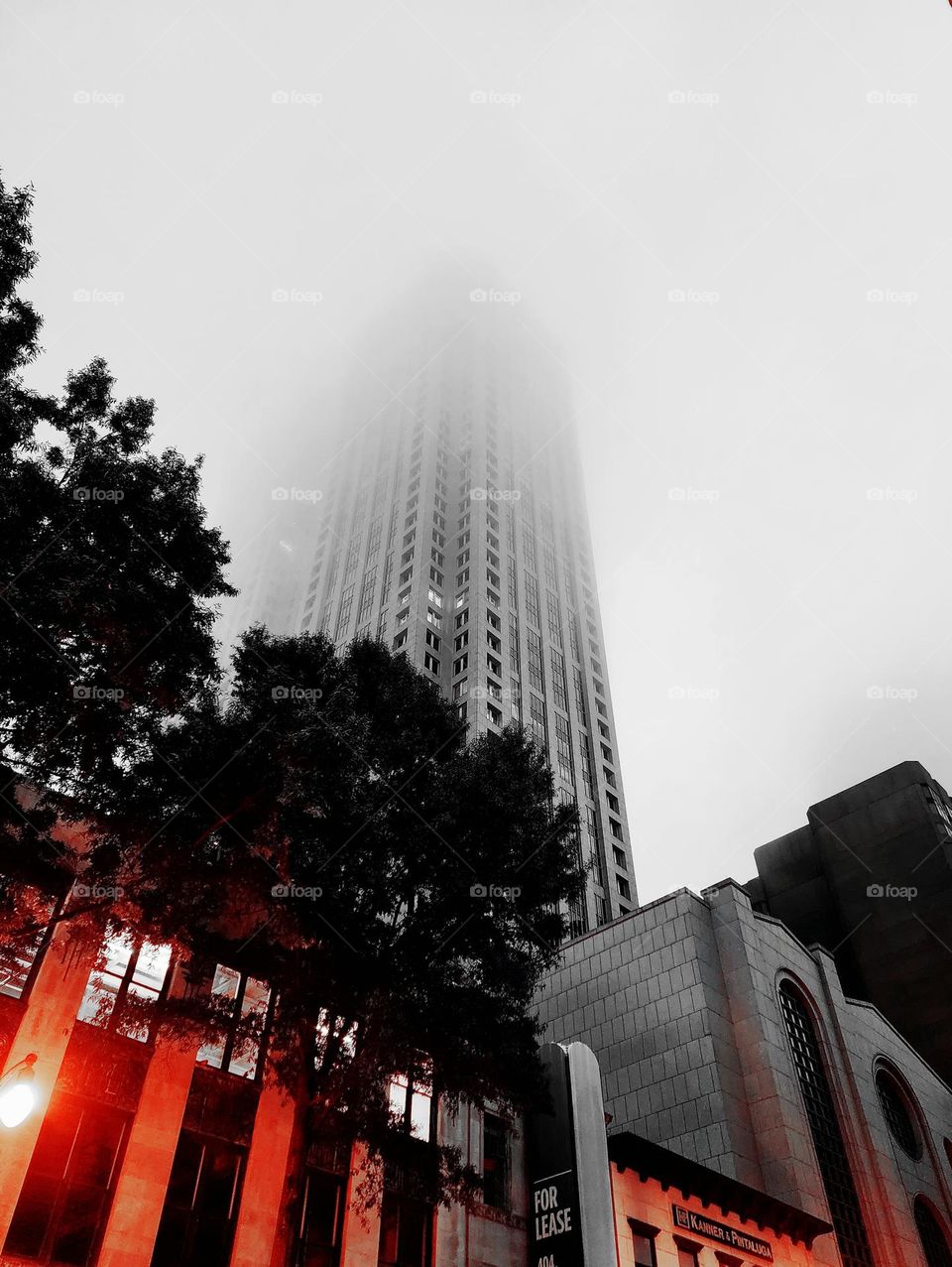 A skyscraper disappears into morning fog as lighting and a filter create a interesting glow