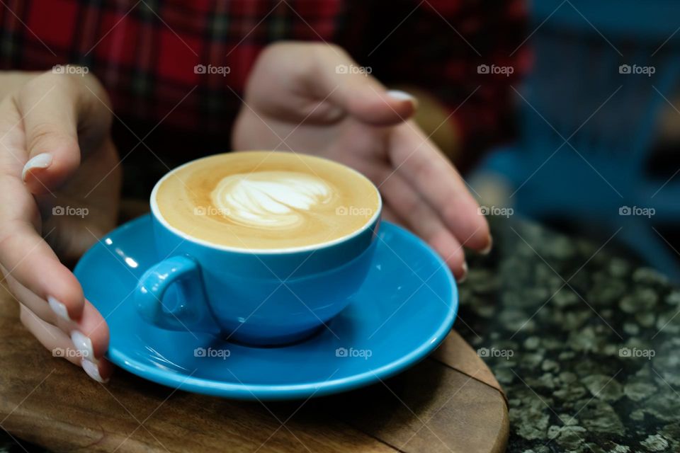 Hands and blue cup of cappuccino
