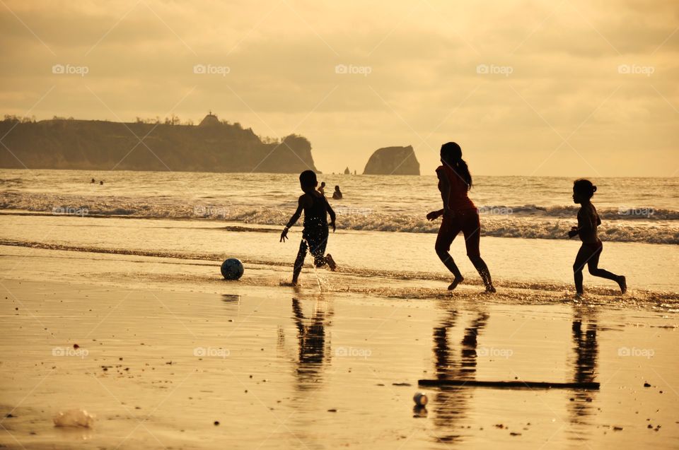 Children playing soccer on the beach at sunset 