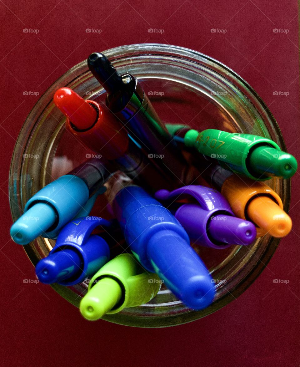 Overhead closeup of colorful pens in glass mason jar on red background 