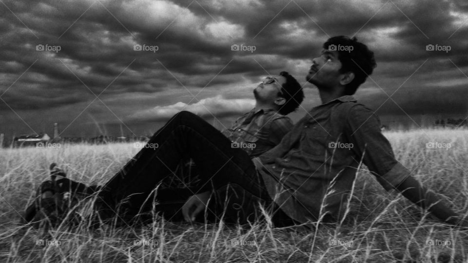 Young indian men on grassy field looking at storm cloud