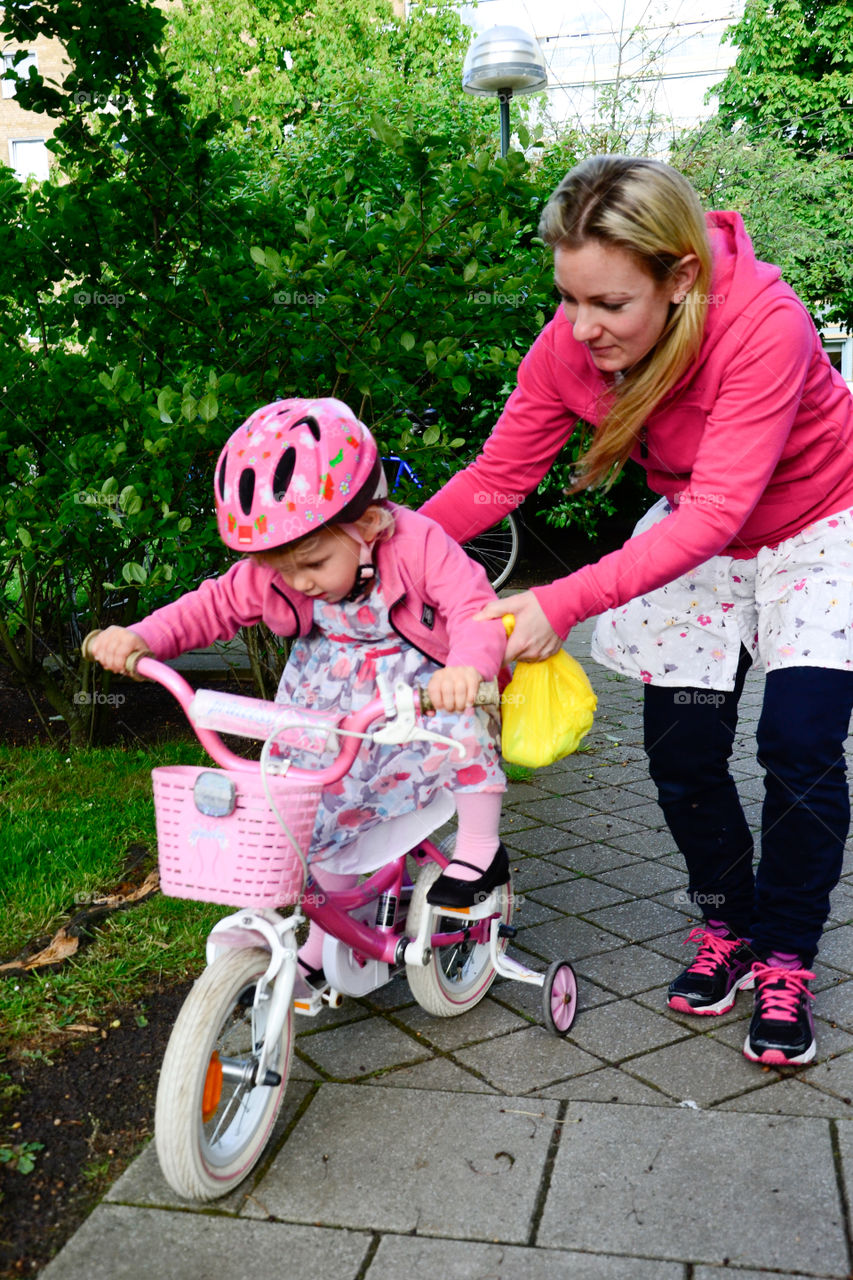 Mom helping her little doughter on her first time on a bike.