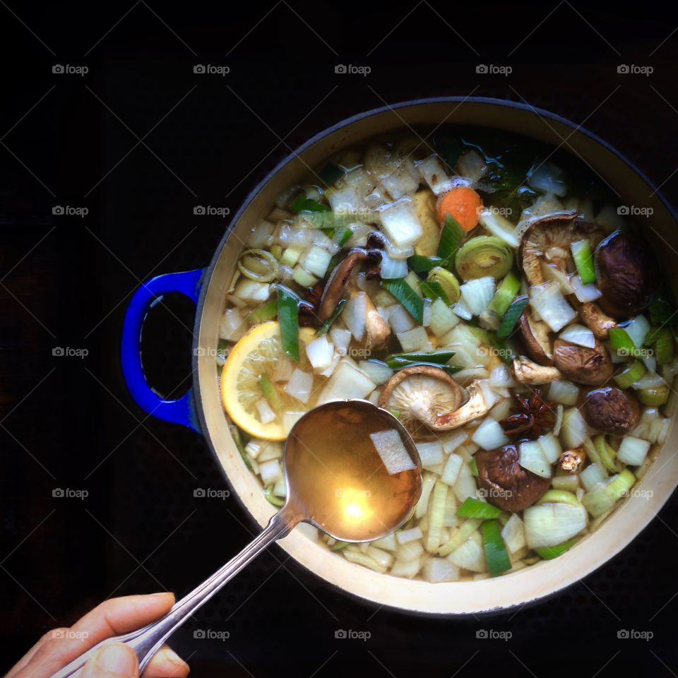Vietnamese Pho Broth cooking in ceramic pot with ladle. 