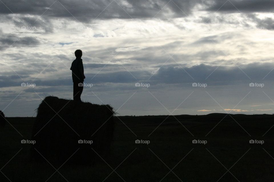 Silhouette of a boy standing on a hay bale