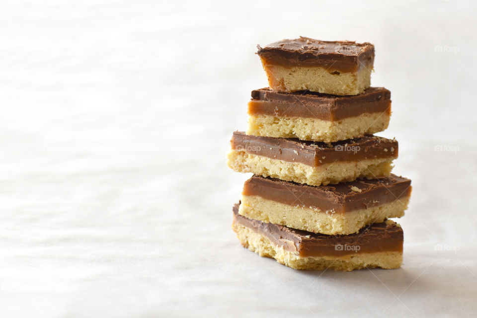Millionaire's shortbread with chocolate and caramel on a parchment paper with copy space on the left side.