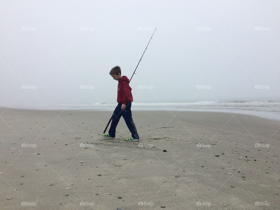 Child fishing pole walking on beach rain storm