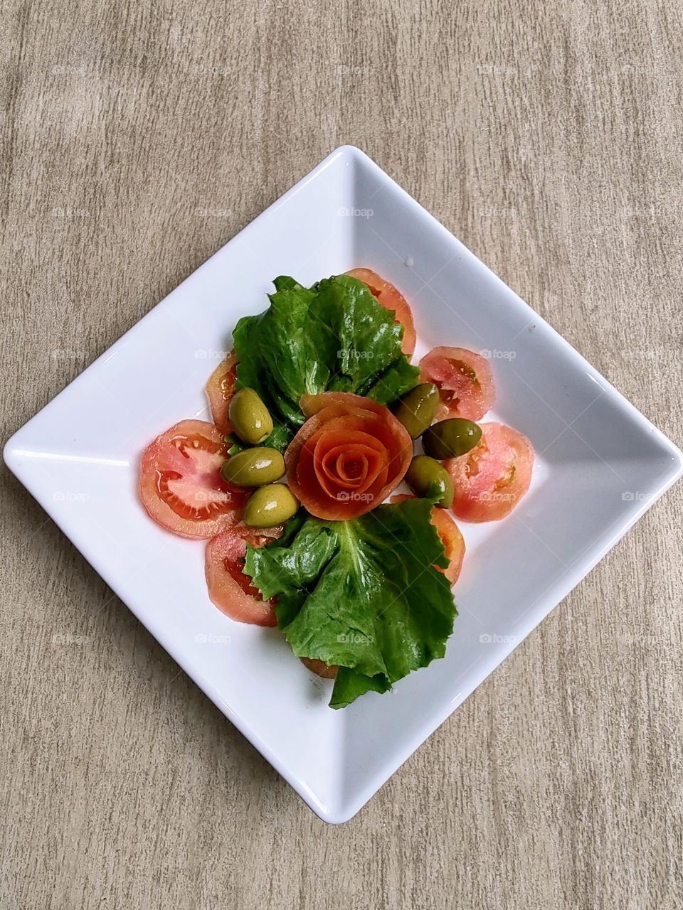 A salad, decorated in a simple way with a tomato flower in the center makes your plate more beautiful.