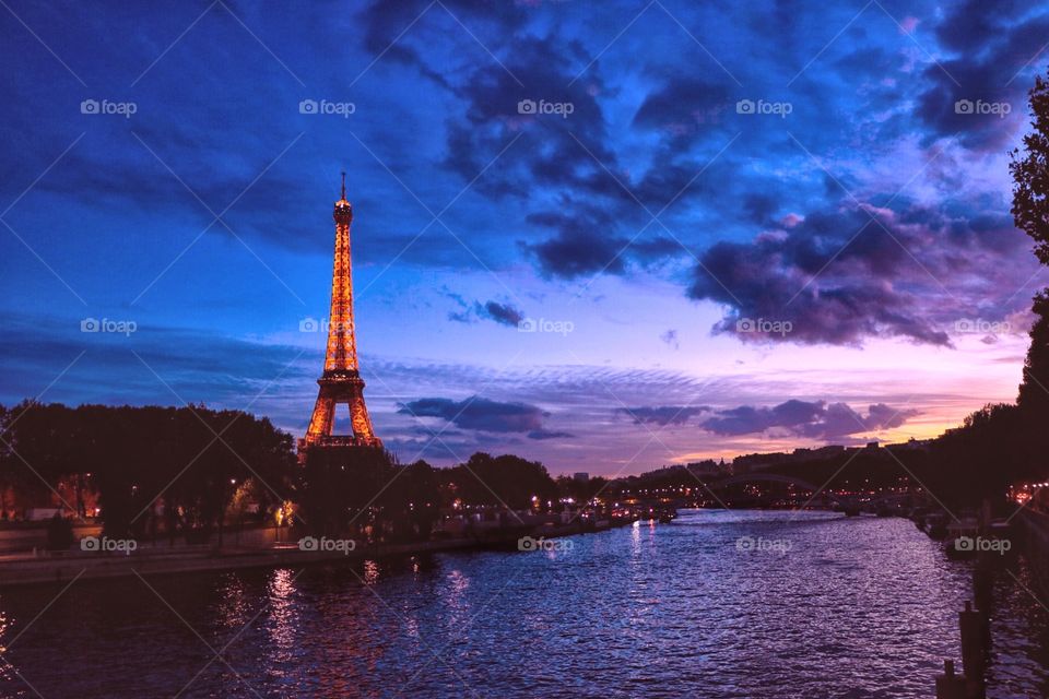 The Eiffel Tower in Paris with a beautiful sunset in the background and the Seine River in the forefront.