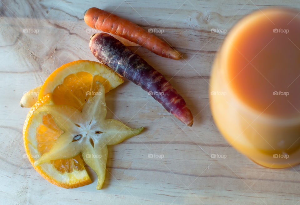 Juicing lifestyle Healthy fruit and vegetable orange carrot and tropical star fruit ingredients on wood table next to tall glass of freshly blended juice 