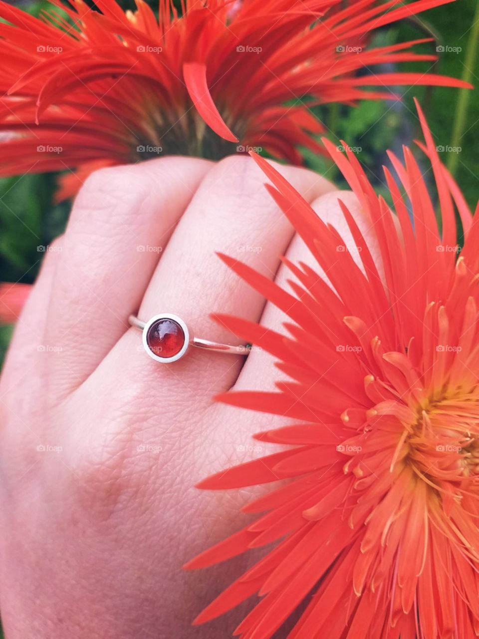 Anel de prata e pedra granada competindo sua cor com a gerbera.