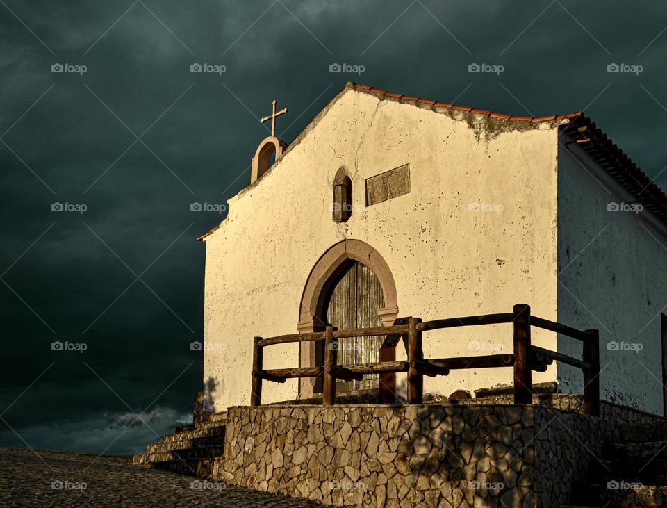 Dark storm clouds gather behind an abandoned church, illuminated by the last rays of sunlight 