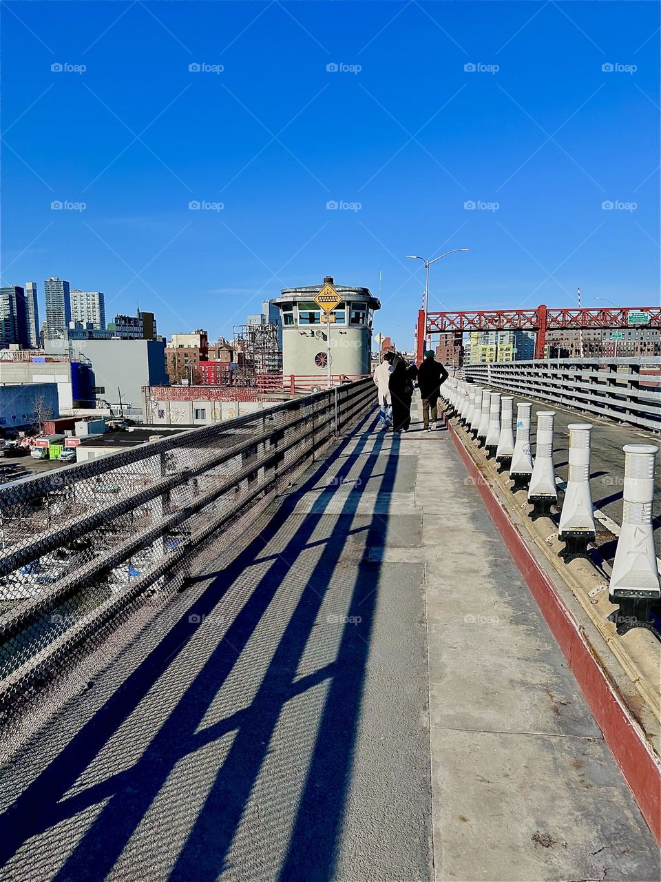 This is the pedestrian lane of the „Pulaski Bridge“ at „Newtown Creek“ that connects „Greenpoint“, Brooklyn to LIC, Queens. We are walking towards LIC and the shadow from the railing provides additional guiding lines. 2024. Hypnotic Productions