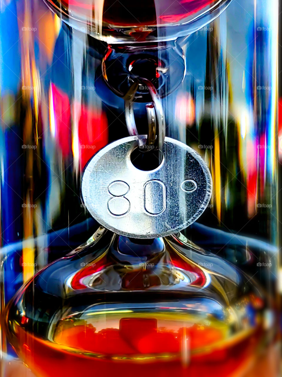 Metal temperature ring on a galileo thermometer with colors reflecting on the cylinder glass.