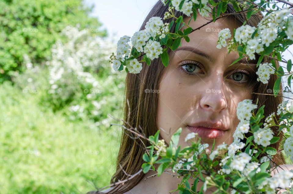 Portrait of beautiful young woman on a clearing among white flowers