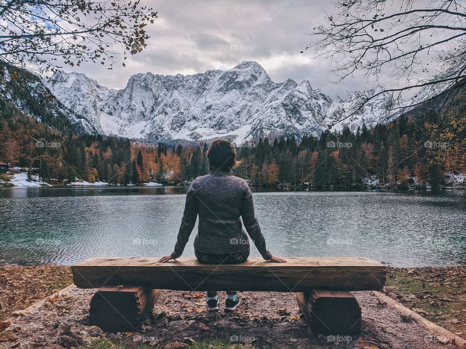 A woman traveler sitting and admires the view of the snow-capped mountain peaks against italian lake.