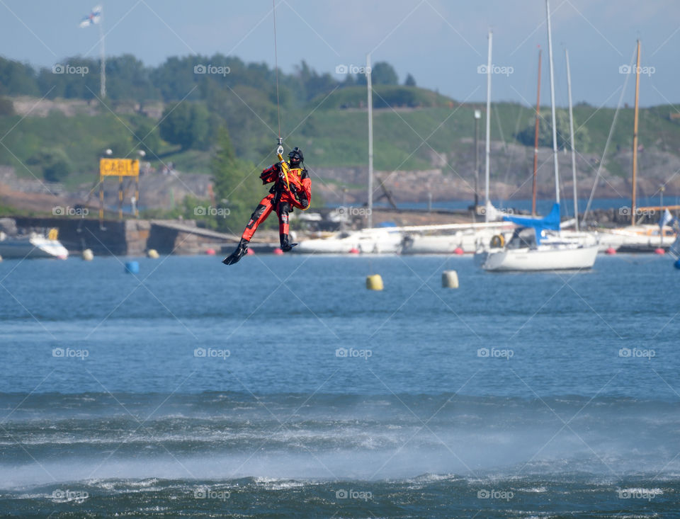 Helsinki, Finland -June 9, 2017: Unidentified Finnish Coast Guard rescue swimmer drops down to the Baltic Sea be a wire in rescue exercise or performance in the Kaivopuisto Air Show 2017 in front of Suomenlinna fortress island on sunny June evening.