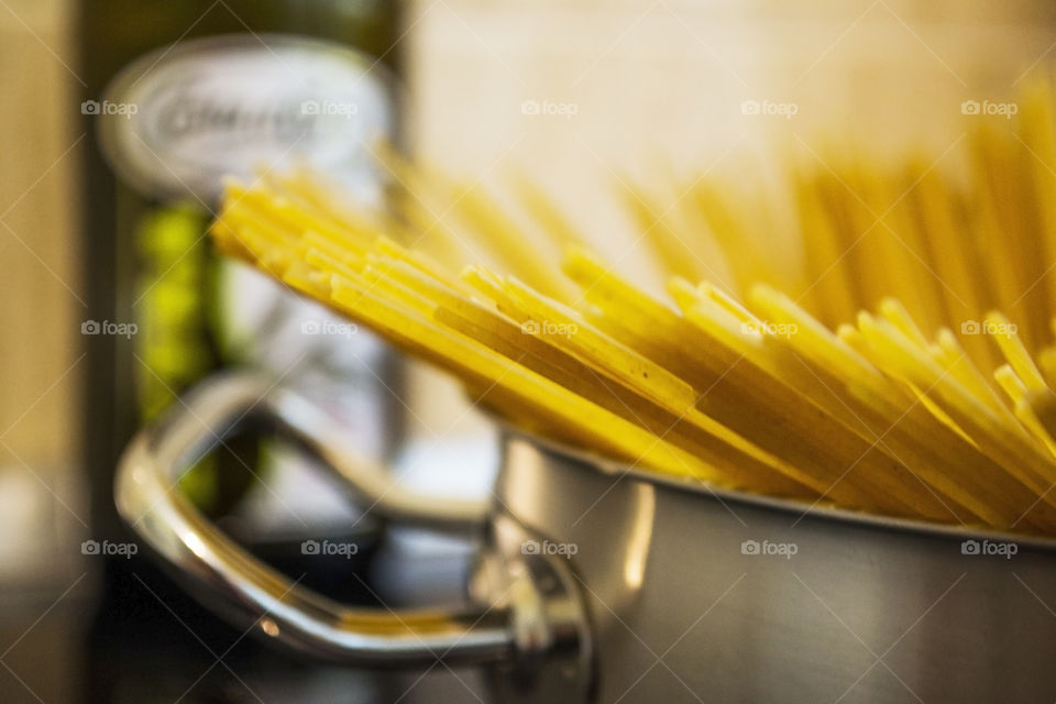 Close-up of spaghetti in a kitchen pot with an olive pup bottle in the background