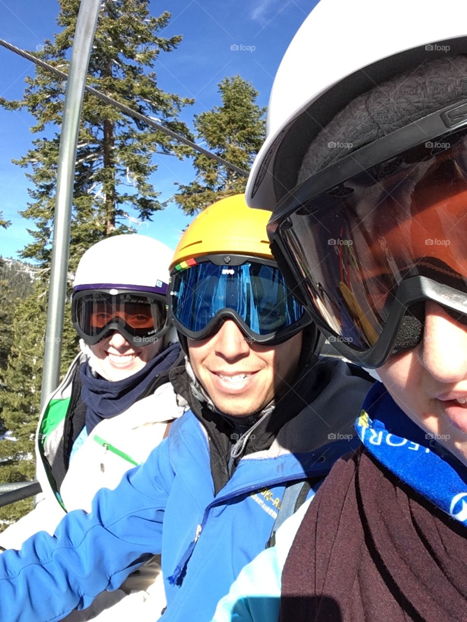 Three people on a chair lift with helmets and ski masks on