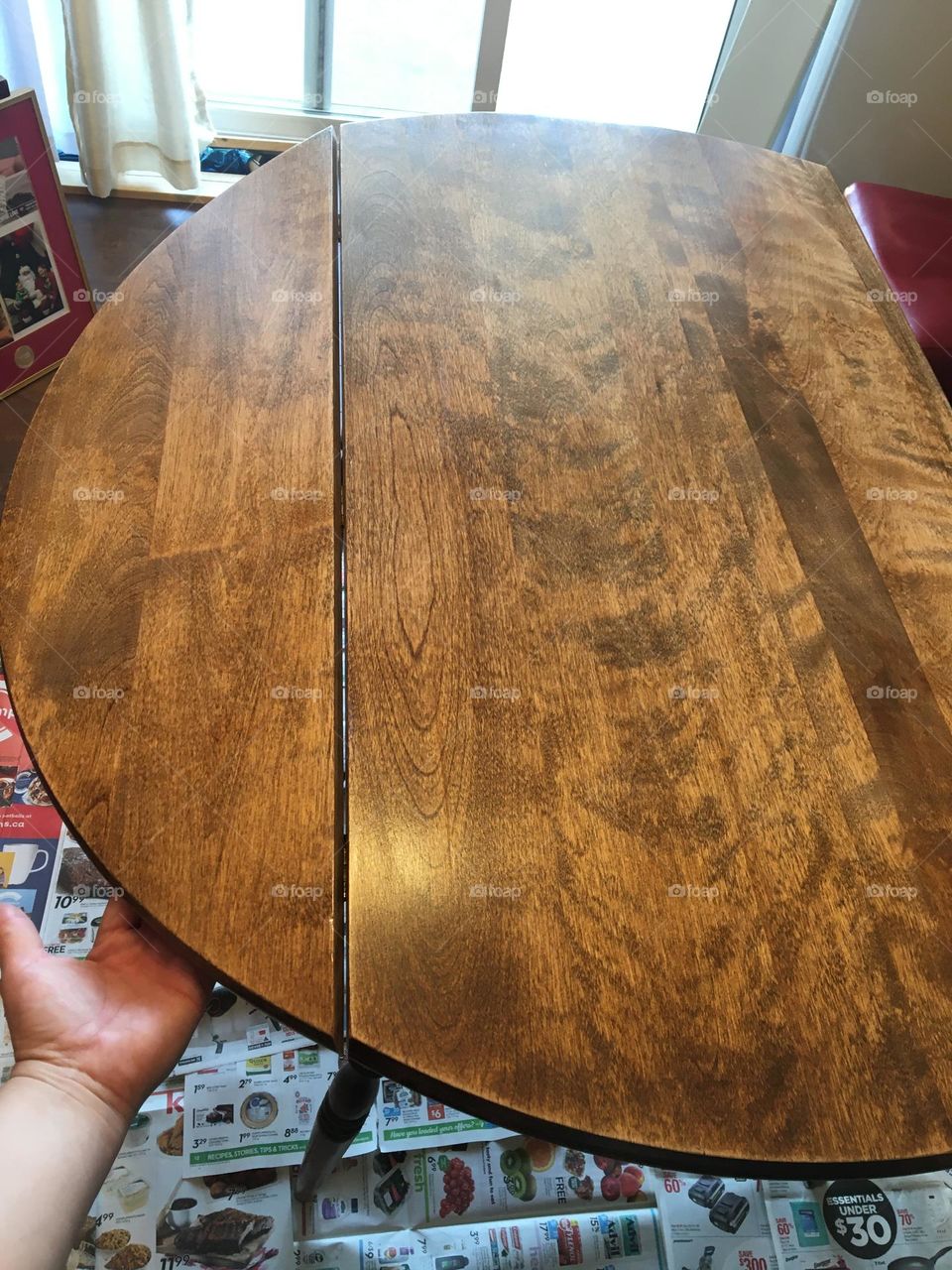A newly varnished wood double drop leaf table, looks all shiny and new again, after my daughter revarnished it, on top of newspapers so she didnt have to worry about the floor, my hand is holding the one side up because it wasn’t dry yet