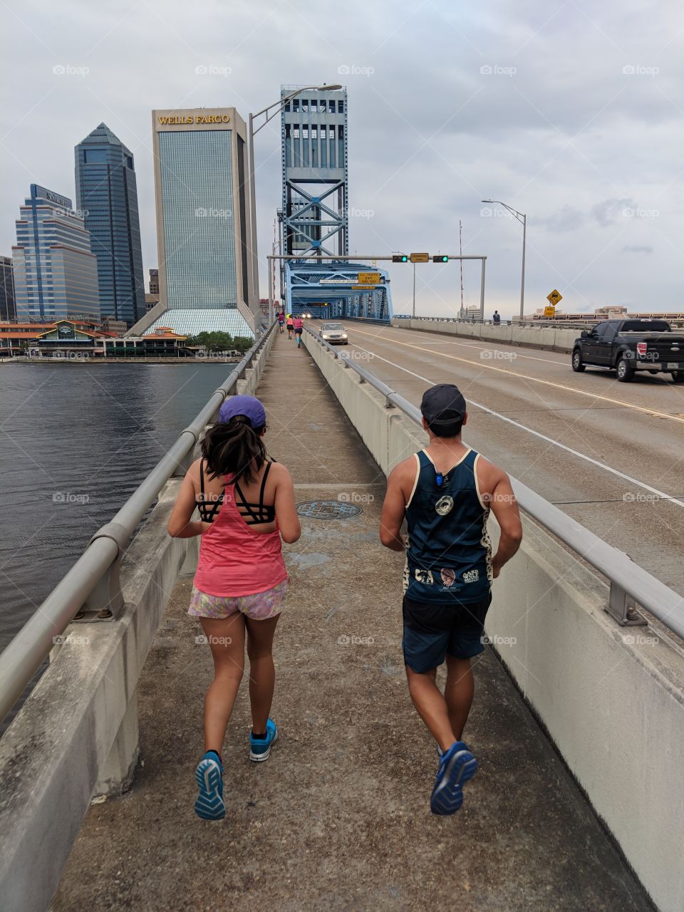 Runners on bridge over water facing the city in an urban landscape. Jacksonville Florida. Blue bridge view.