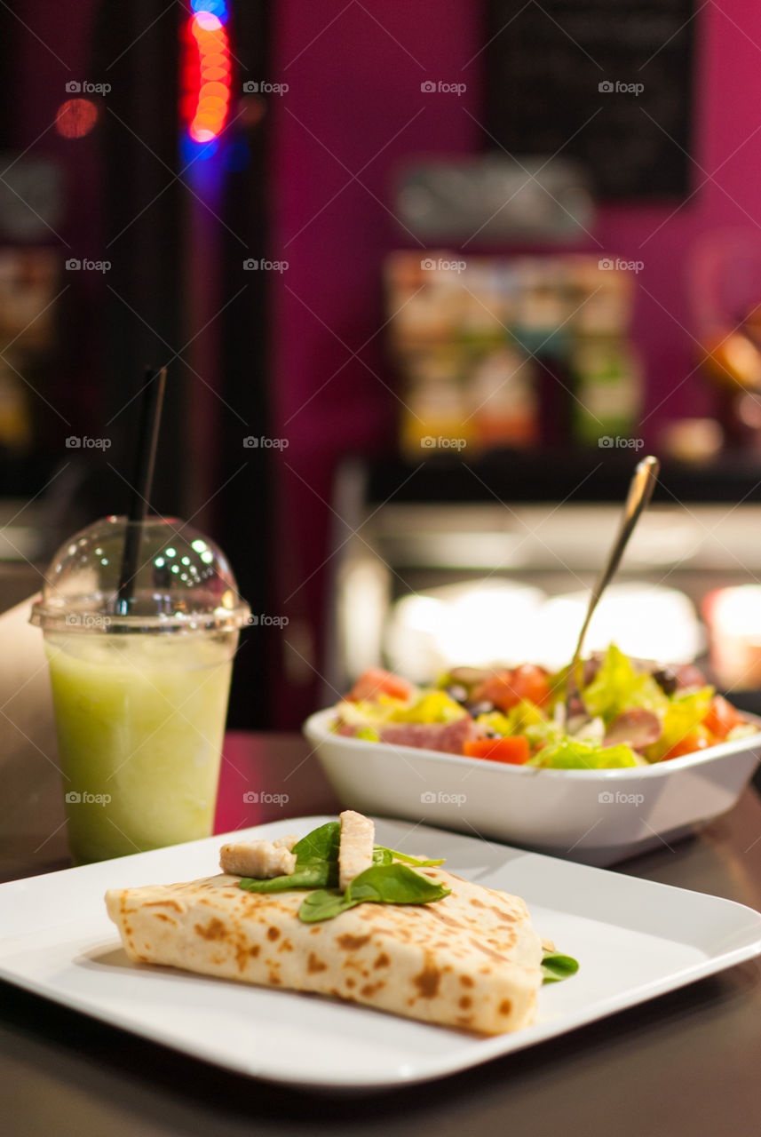 chicken quesadilla with side salad and green apple/pear smoothie in foreground with cafe blurred in background