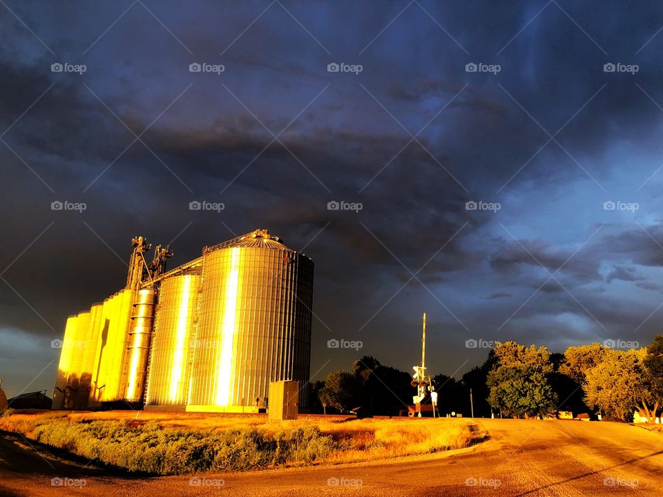 Natural light from sunset illuminates grain elevators against the backdrop of a post storm