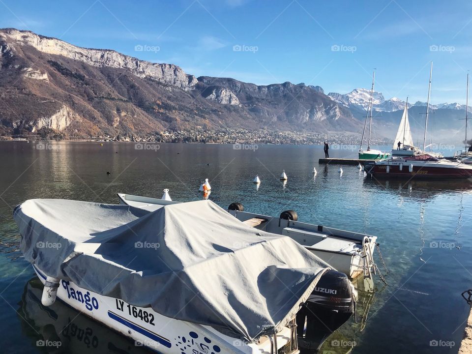Taken in Annecy, France. A lovely and beautiful clear lake (Lake Annecy) featuring mountains, and a boat 